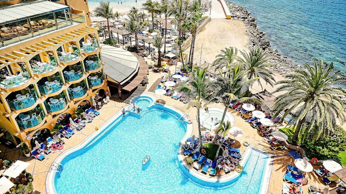 Hotellin uima-allas rannalla, ympärillä palmuja ja aurinkotuoleja. (Tekoälyn luoma teksti)