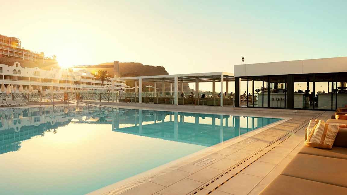 Ulkouima-allas hotellissa, jossa on aurinkotuoleja ja rakennus taustalla. (Tekoälyn luoma teksti)