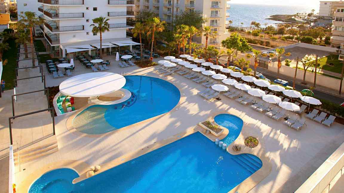 Hotellialue lähellä merta, jossa on uima-allas, aurinkotuoleja ja aurinkovarjoja. (Tekoälyn luoma teksti)