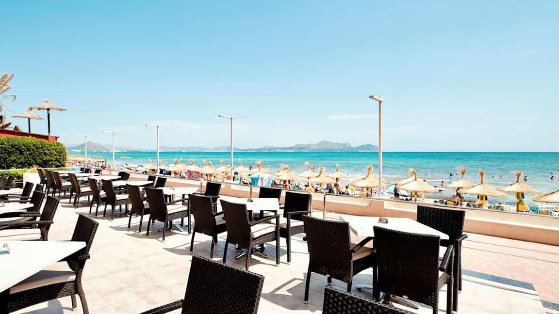 Ulkoravintola, josta näkymä hiekkarannalle ja merelle, varjoja. (Tekoälyn luoma teksti)