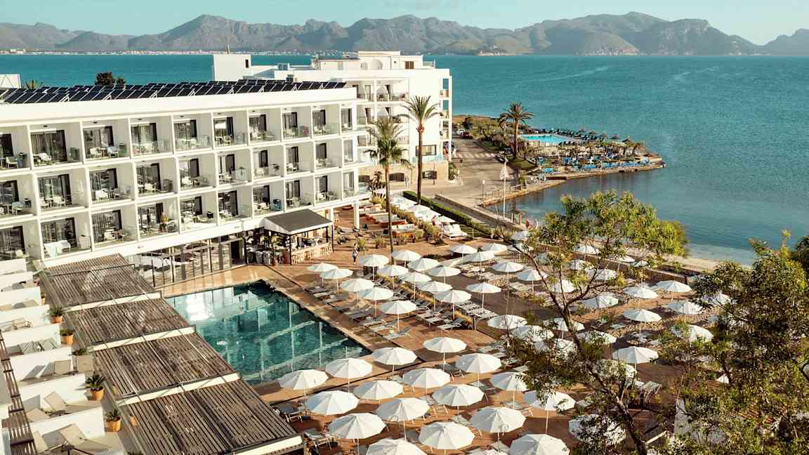 Hotellialue meren rannalla, aurinkotuoleja ja aurinkovarjoja uima-altaan ympärillä. (Tekoälyn luoma teksti)