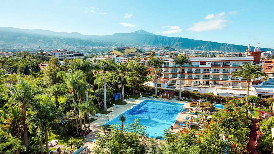 Uima-allas, jota ympäröivät kasvit ja rakennukset, taustalla vuori. (Tekoälyn luoma teksti)