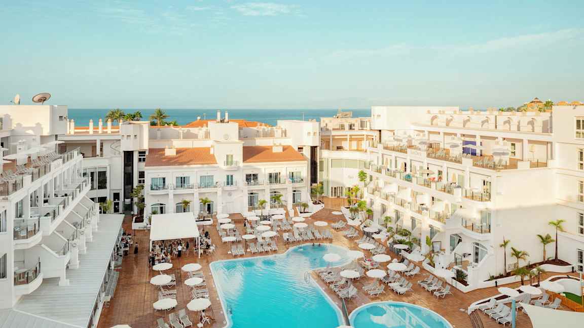 Näkymä hotellialueelle, jossa uima-allas ja aurinkotuoleja, taustalla näkyy meri. (Tekoälyn luoma teksti)