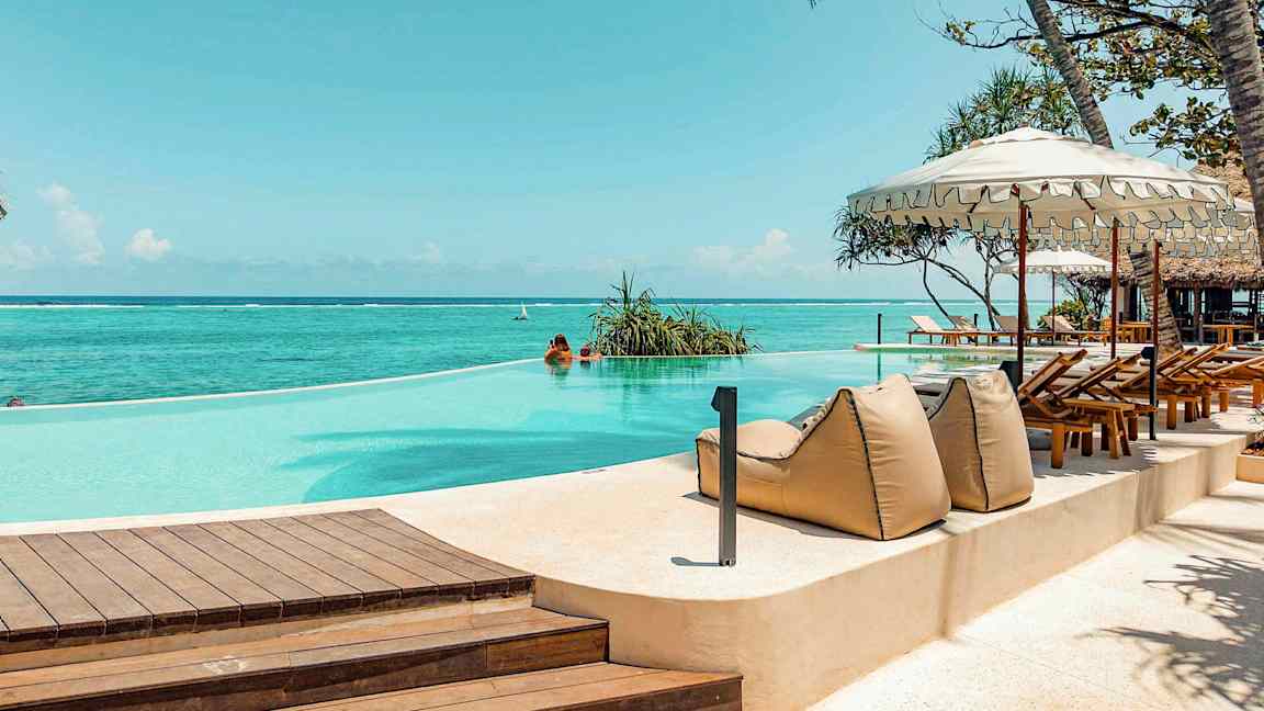 Infiniteettiuima-allas meren äärellä, ympäröity aurinkotuoleilla ja varjoilla. (Tekoälyn luoma teksti)