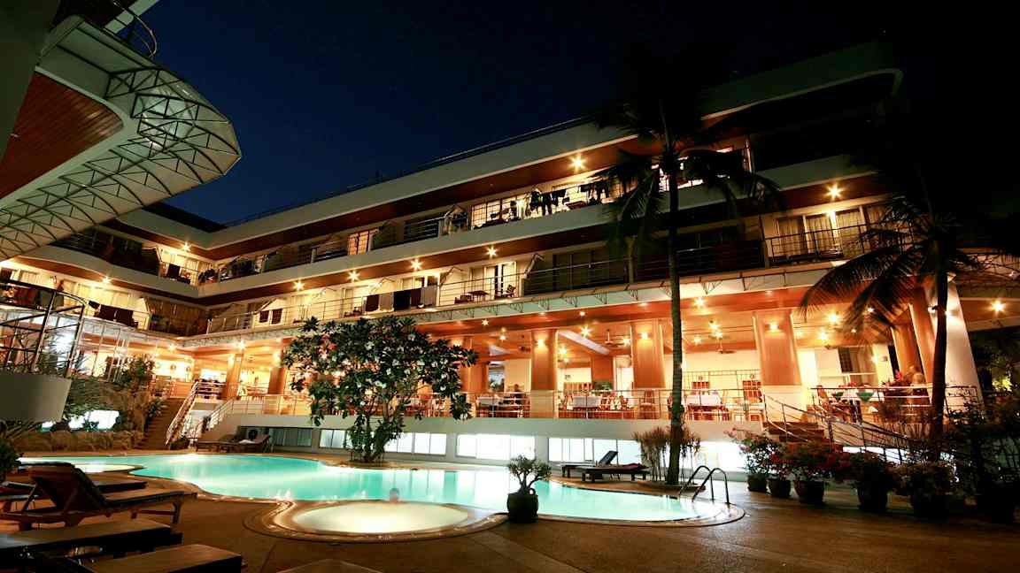 Ilta näkymä monikerroksisesta rakennuksesta, valaistu julkisivu ja uima-allas etualalla. (Tekoälyn luoma teksti)