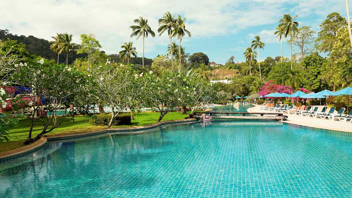 Uima-allas, jota ympäröivät aurinkotuolit, varjot ja palmupuut. (Tekoälyn luoma teksti)