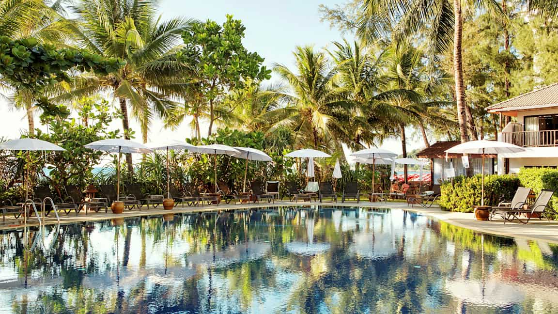 Ulkouima-allas, jota ympäröivät aurinkotuolit ja aurinkovarjot, taustalla palmuja. (Tekoälyn luoma teksti)