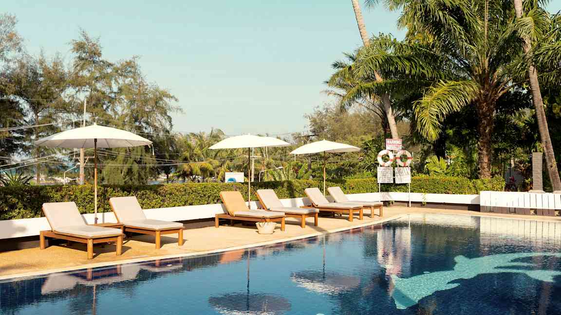 Ulkouima-allas, jossa on aurinkotuoleja ja sateenvarjoja. Taustalla trooppisia puita. (Tekoälyn luoma teksti)