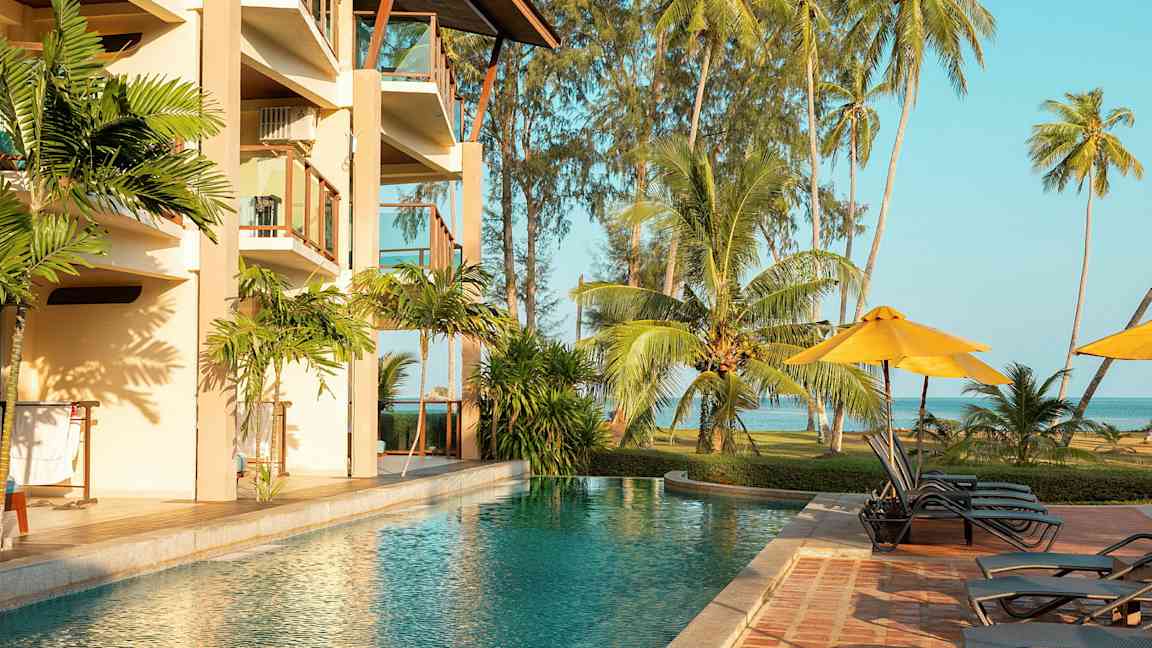 Ulkoallas hotellin vieressä, jossa on parvekkeita, ympäröity trooppisilla palmupuilla ja nurmikolla meren äärellä. (Tekoälyn luoma teksti)