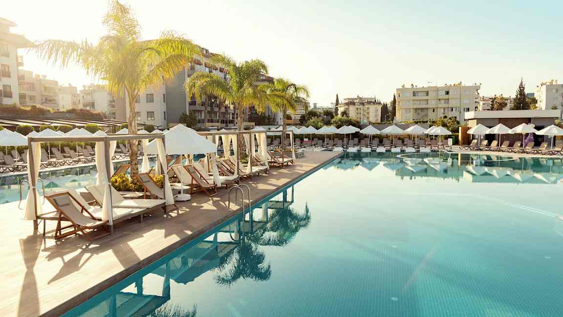 Uima-allas, jossa aurinkotuoleja ja aurinkovarjoja lomakeskuksen ympäristössä. (Tekoälyn luoma teksti)