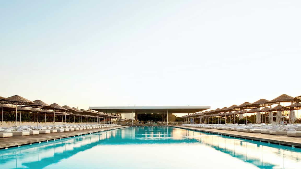 Suuri ja pitkä uima-allas, jonka molemmin puolin on aurinkovarjoja ja aurinkotuoleja. (Tekoälyn luoma teksti)