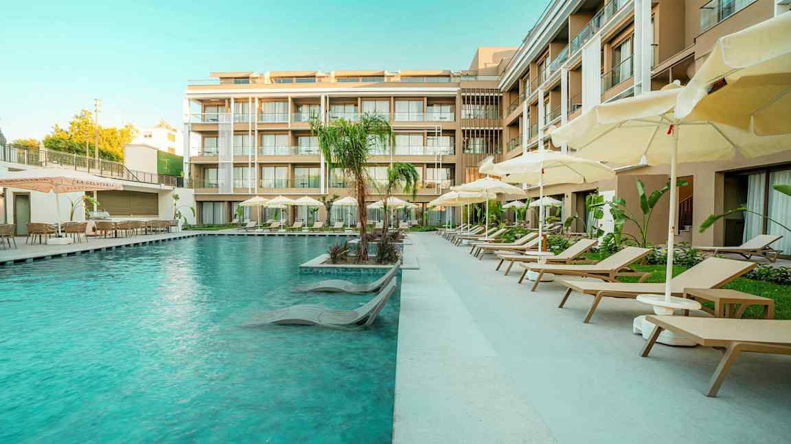 Hotellin uima-allas, jonka vieressä aurinkotuoleja ja varjoja nykyaikaisten rakennusten vierellä. (Tekoälyn luoma teksti)