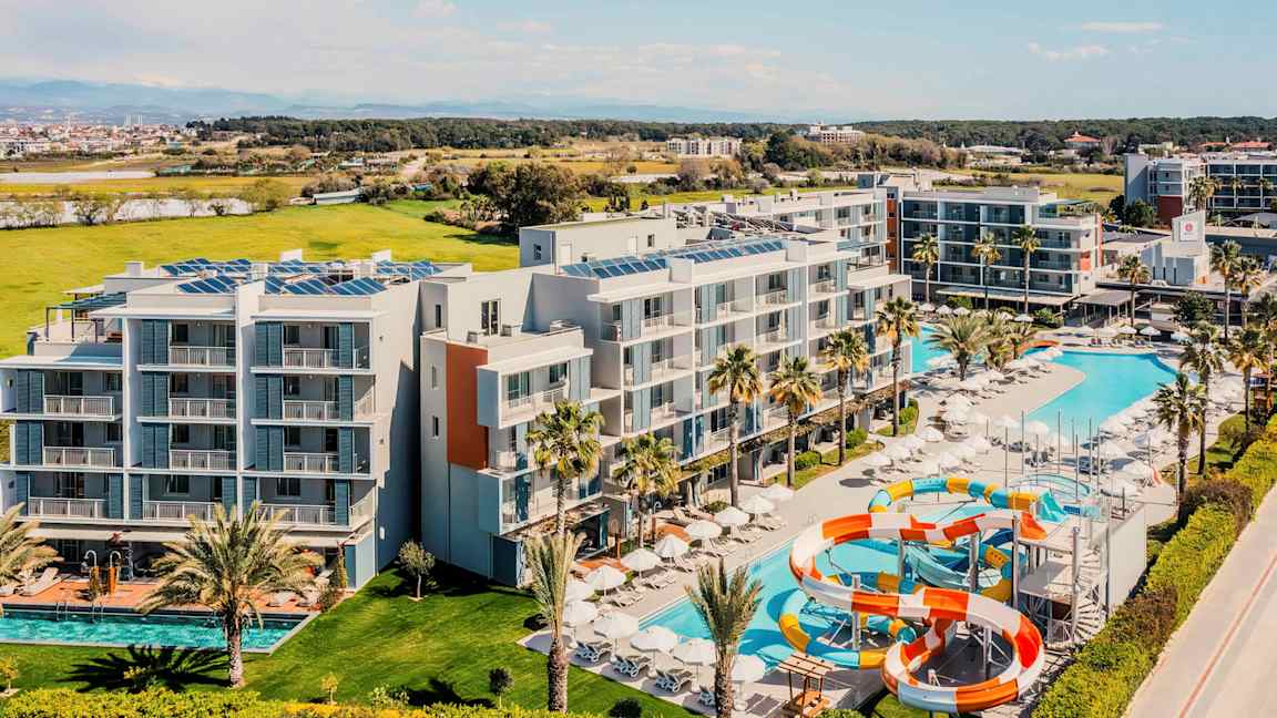 Ilmakuva hotellista, jossa on uima-altaita ja vesiliukumäkiä, ympäröitynä viheralueilla. (Tekoälyn luoma teksti)