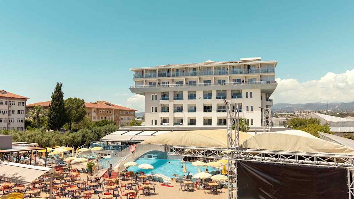 Kuva monikerroksisesta hotellista, uima-allasalueesta aurinkotuoleilla, aurinkovarjoilla ja rentoutumisalueella. (Tekoälyn luoma teksti)