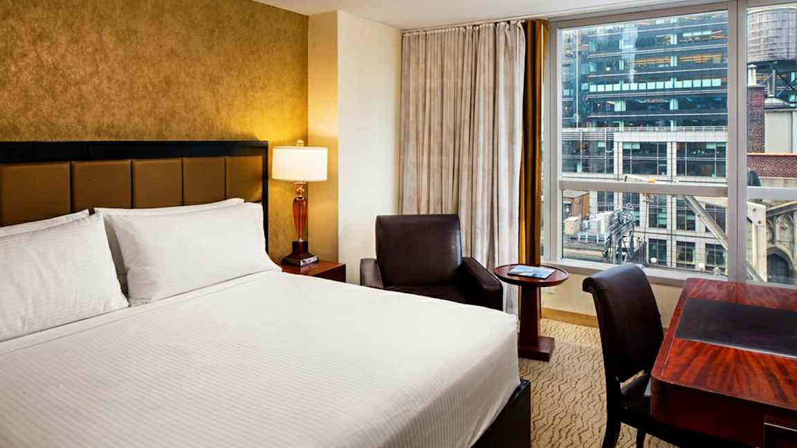 Hotellihuone, jossa on parisänky, kirjoituspöytä ja nojatuoli. (Tekoälyn luoma teksti)