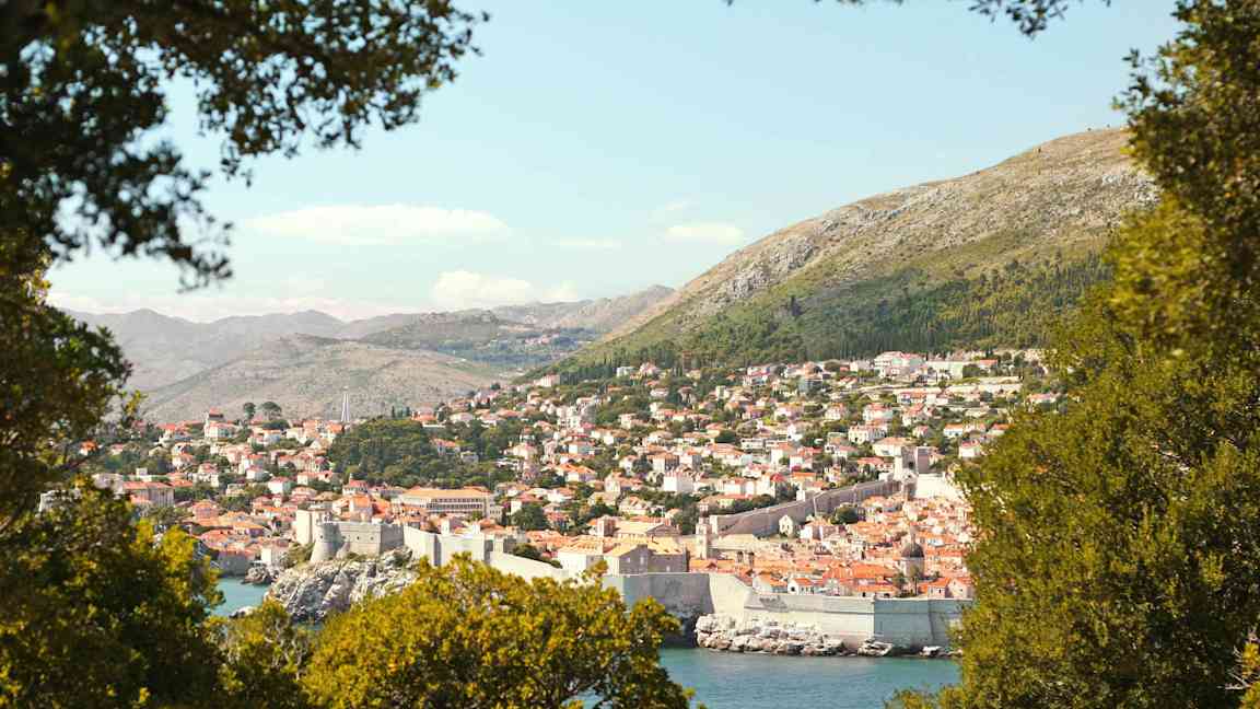 Näköala Dubrovnikiin, jossa näkyy historiallinen kaupunginmuuri, vehreyden ympäröimänä. (Tekoälyn luoma teksti)