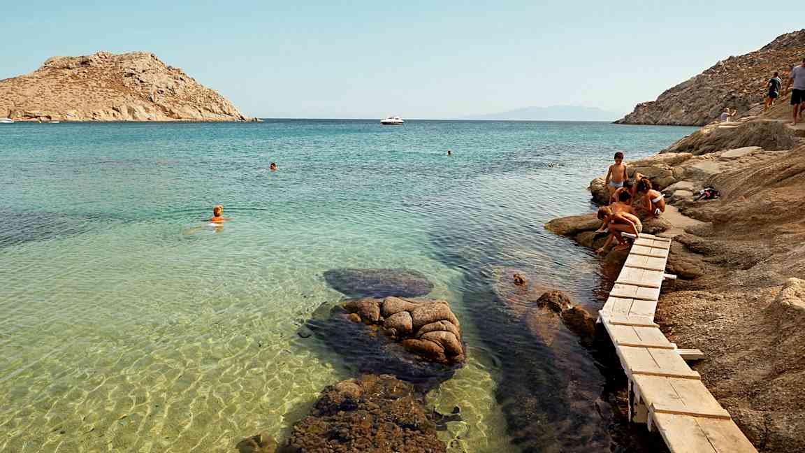 Henkilöitä kallion äärellä lähellä kirkasta sinistä lahtea, jossa uidaan. (Tekoälyn luoma teksti)