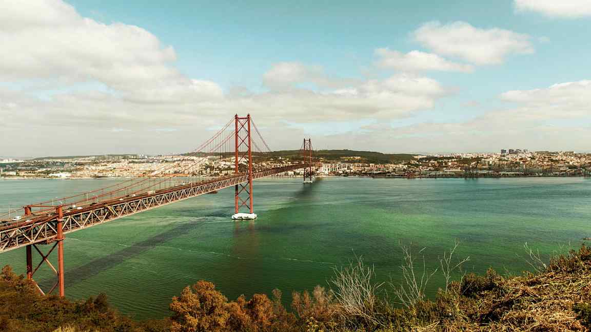 Kuvassa näkyy punainen silta veden päällä, taustalla oleva kaupunki. (Tekoälyn luoma teksti)