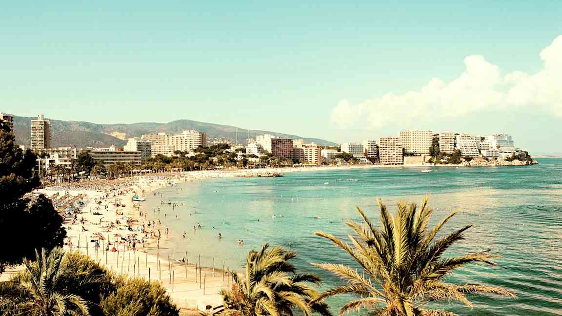 Ranta meren rannalla, ympärillä rakennuksia ja palmuja. (Tekoälyn luoma teksti)