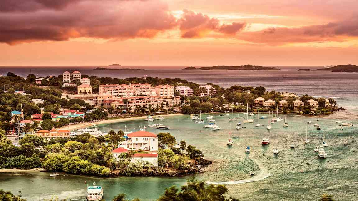 Kuva rannikkokaupungista, jossa on veneitä satamassa, ympärillä vihreitä puita ja taustalla auringonlasku. (Tekoälyn luoma teksti)