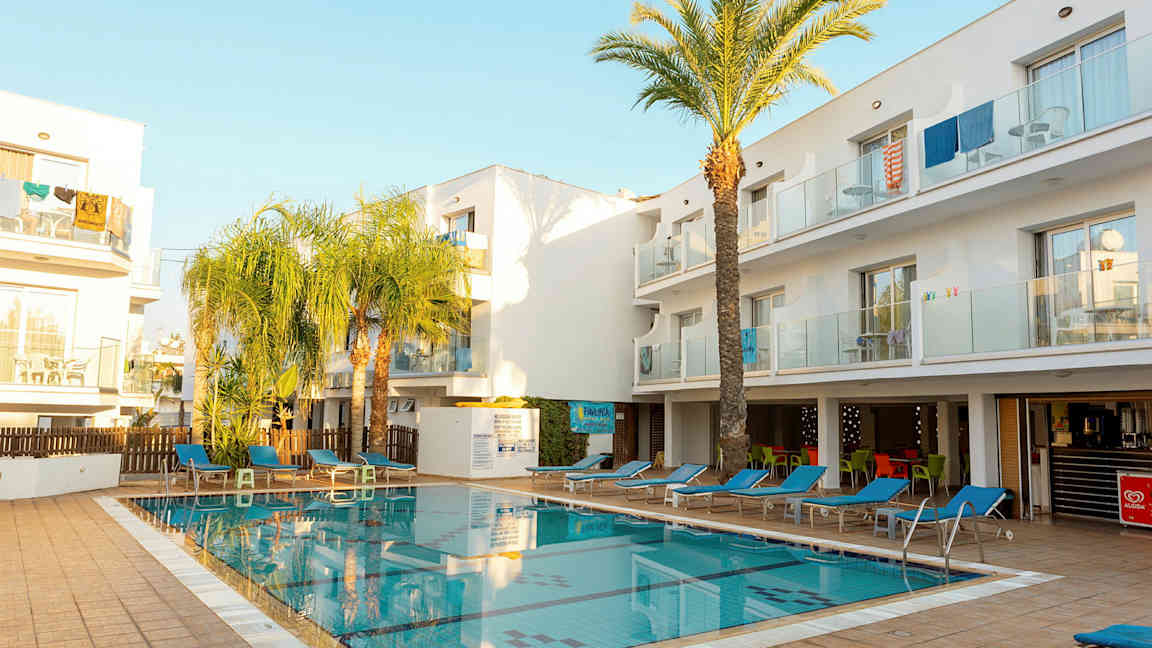 Ulkoallas, jota ympäröivät aurinkotuolit ja valkoiset rakennukset. (Tekoälyn luoma teksti)