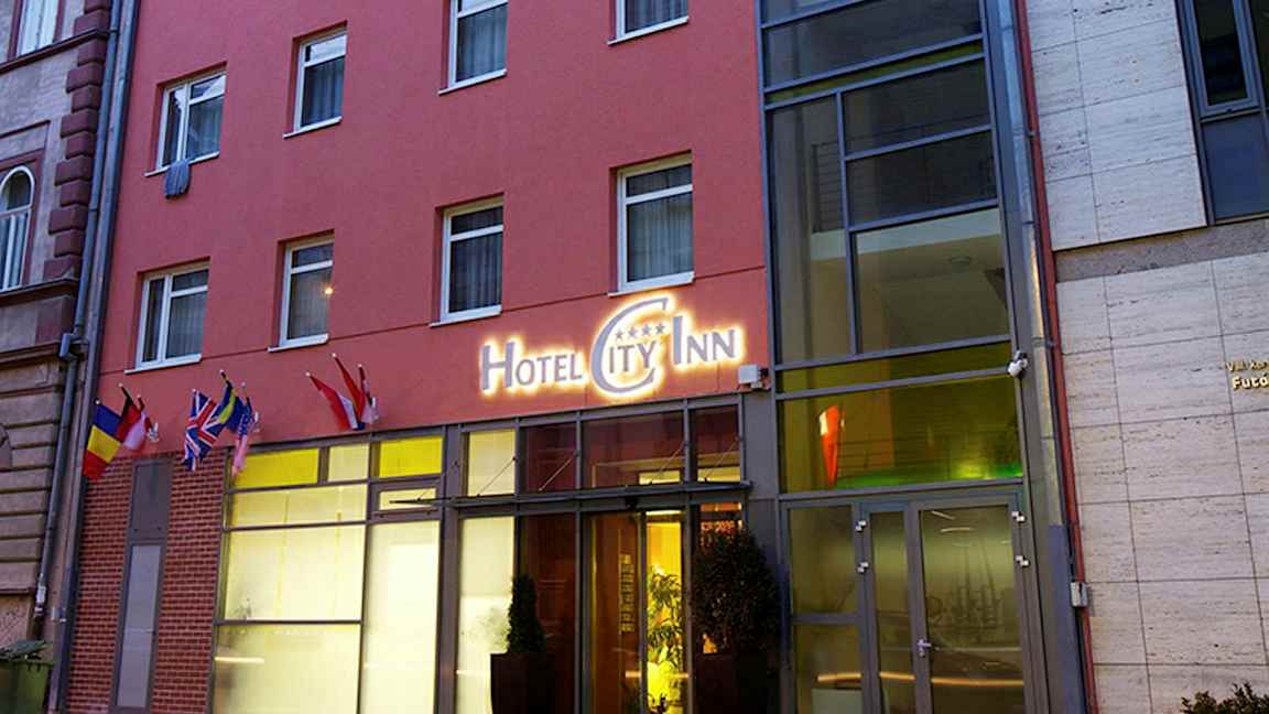 Hotellirakennuksen ulkopuolella kyltti, jossa lukee "Hotel City Inn", sekä useita lippuja sisäänkäynnin luona. (Tekoälyn luoma teksti)