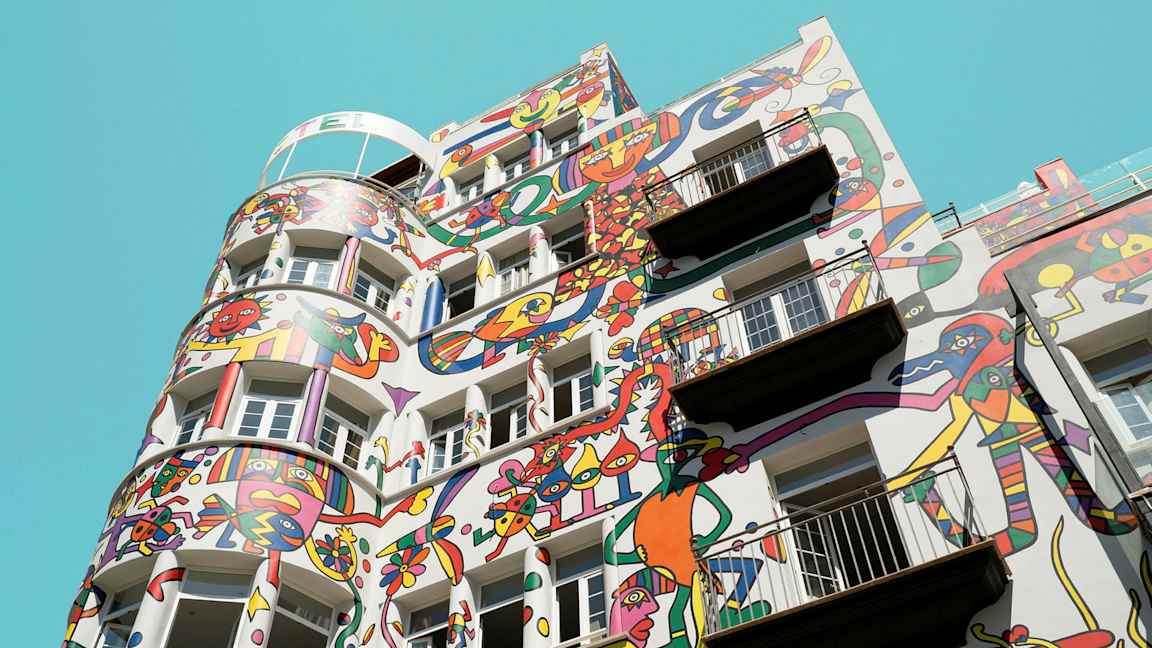 Rakennus, jossa värikkäitä abstrakteja maalauksia julkisivussa kirkkaan sinistä taivasta vasten. (Tekoälyn luoma teksti)