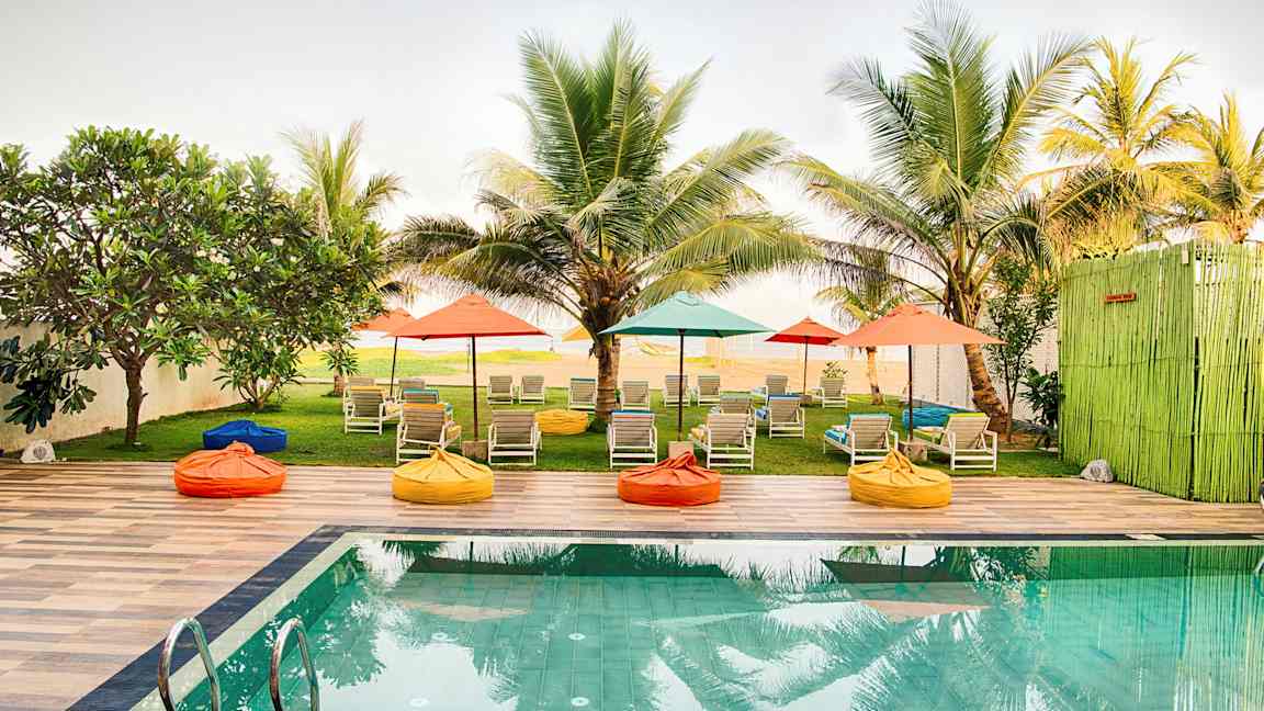 Uima-allas, jossa on aurinkotuoleja ja värikkäitä varjoja palmujen ympäröimässä puutarhassa. (Tekoälyn luoma teksti)