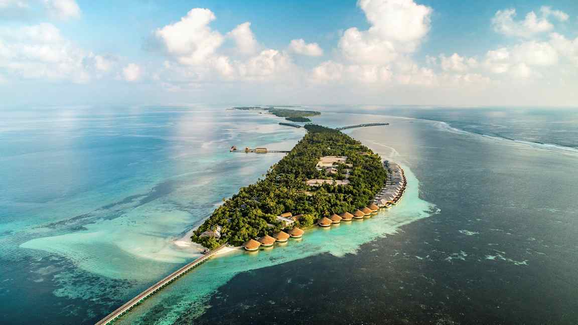 Ilmakuva trooppisesta saaresta, jossa veden päällä sijaitsevia huviloita ja turkoosia merta. (Tekoälyn luoma teksti)