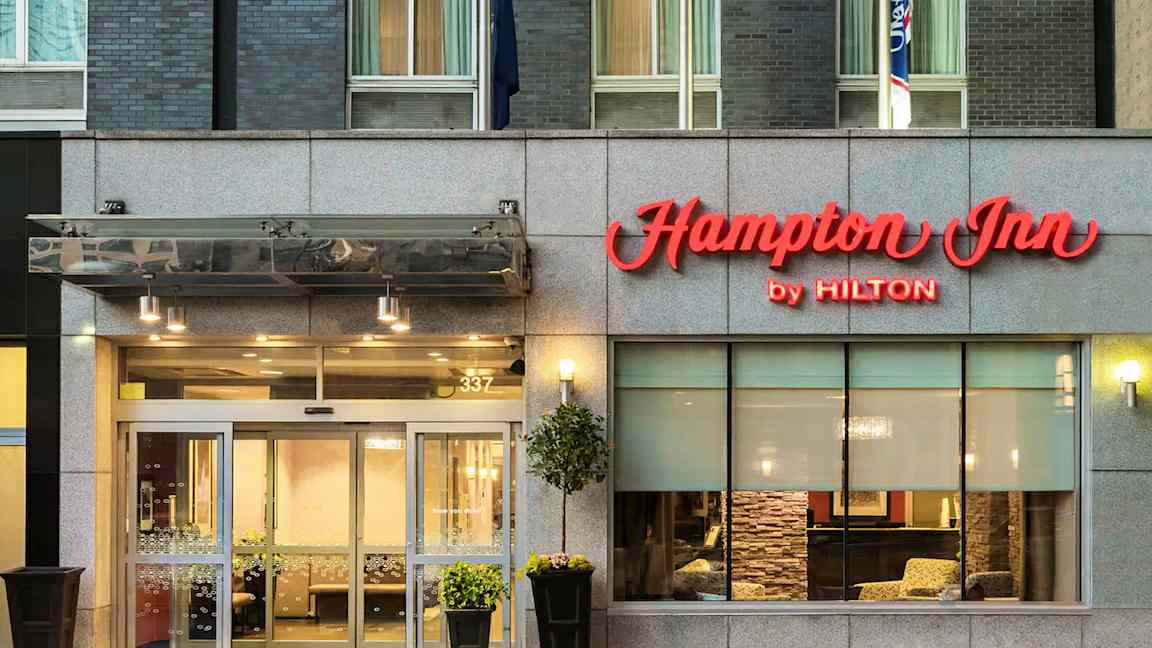 Hotellin sisäänkäynti, jonka yläpuolella lukee "Hampton Inn by Hilton". (Tekoälyn luoma teksti)