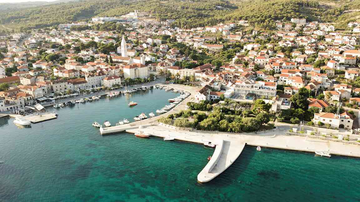 Ilmakuva rannikkokaupungista, jossa veneitä satamassa ja punakattoisia taloja. (Tekoälyn luoma teksti)