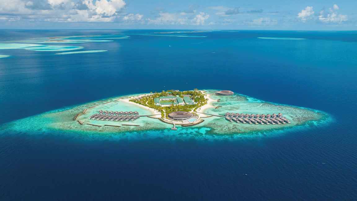 Ilmakuva trooppisesta saaresta, jossa on lomakeskus ja vedenpäällisiä bungalow-asuntoja. (Tekoälyn luoma teksti)