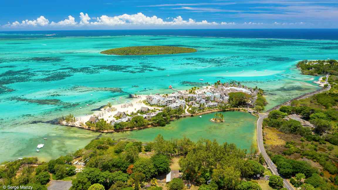 Ilmakuva lomakohteesta rannalla, turkoosin veden ja vehreyden ympäröimänä. (Tekoälyn luoma teksti)