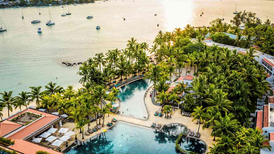 Rantalomakeskus, jossa uima-allas palmujen ja aurinkotuolien ympäröimänä lähellä merta. (Tekoälyn luoma teksti)