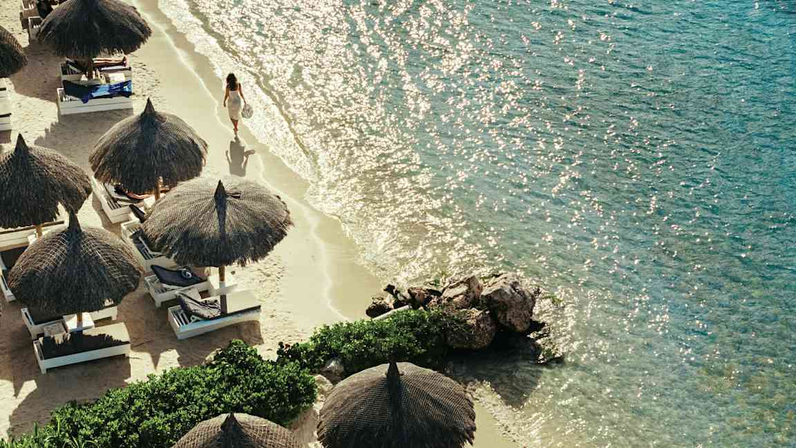 Hiekkaranta, jossa on aurinkovarjoja ja aurinkotuoleja kirkkaan meren äärellä. (Tekoälyn luoma teksti)