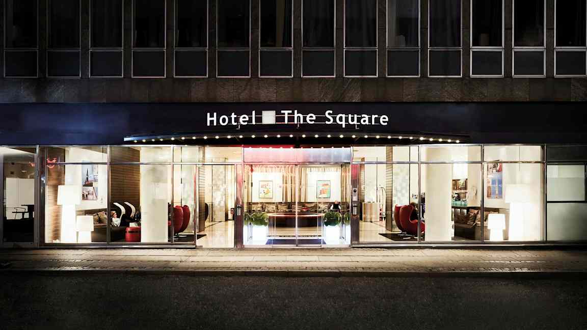 Hotel The Squaren julkisivu ja pääsisäänkäynti, jossa on lasiovet ja suuret ikkunat. (Tekoälyn luoma teksti)