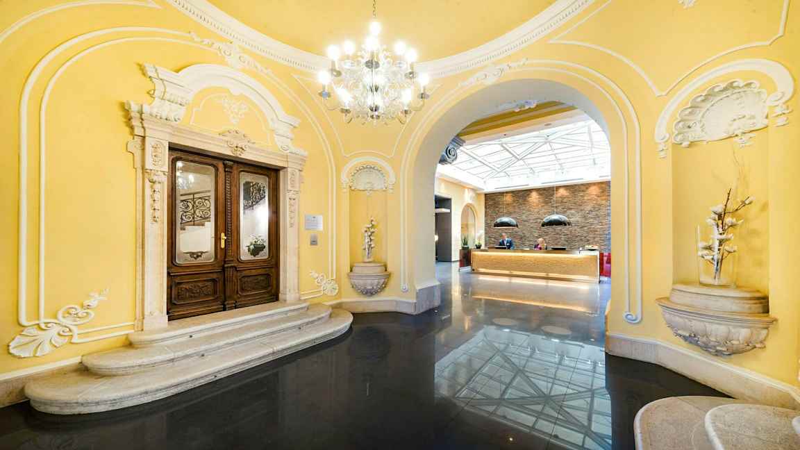 Sisäänkäyntialue klassisilla arkkitehtonisilla yksityiskohdilla ja vastaanotto valoisassa ympäristössä. (Tekoälyn luoma teksti)