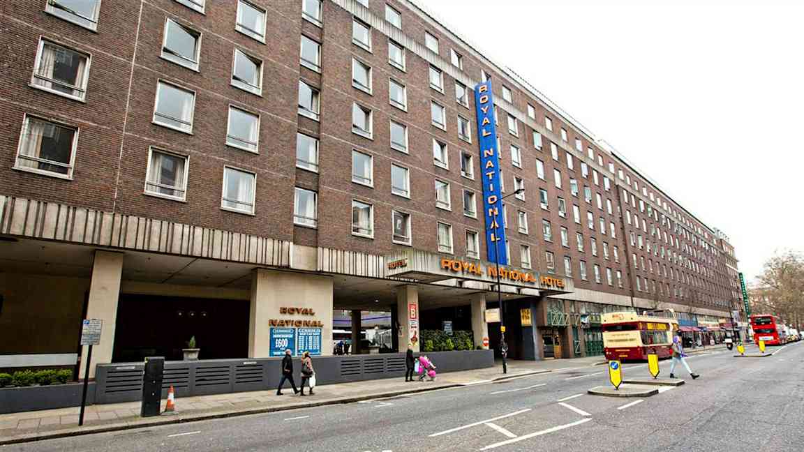 Kuva Royal National Hotellista kadulta, jossa näkyy useita busseja ja jalankulkijoita. (Tekoälyn luoma teksti)