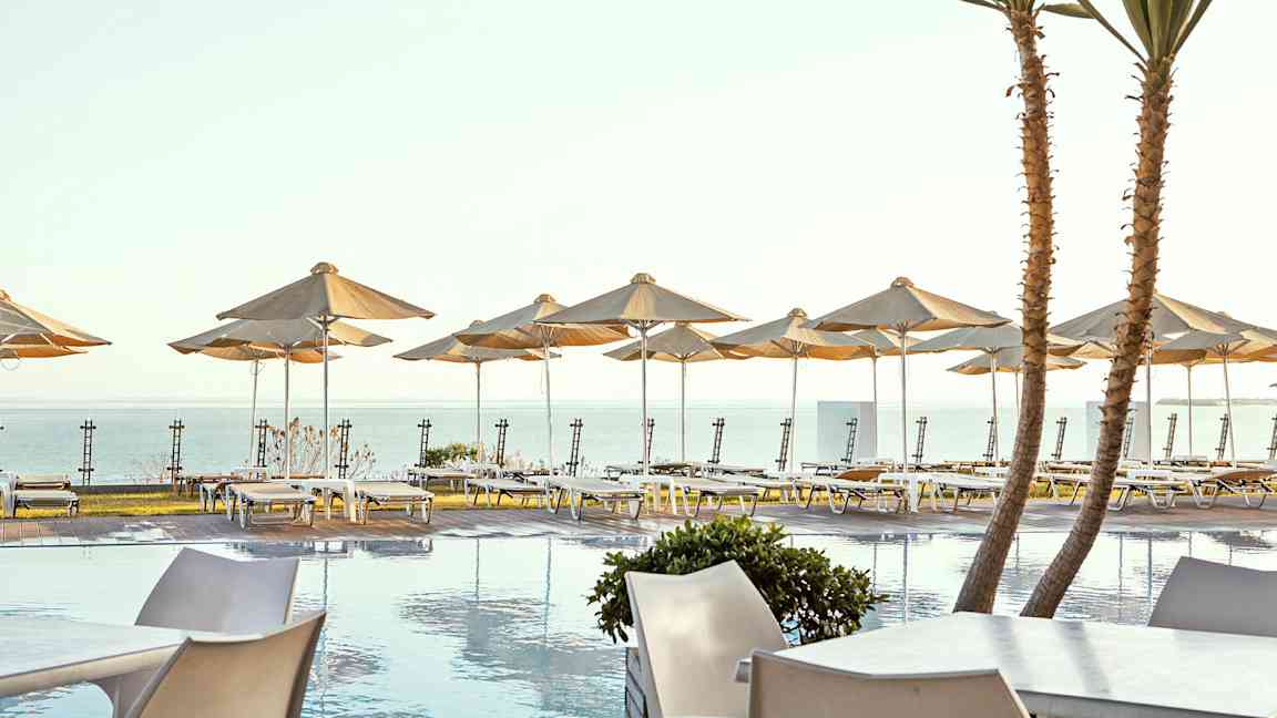 Aurinkoterassi altaalla ja aurinkotuoleja sekä varjoja meren rannalla. (Tekoälyn luoma teksti)