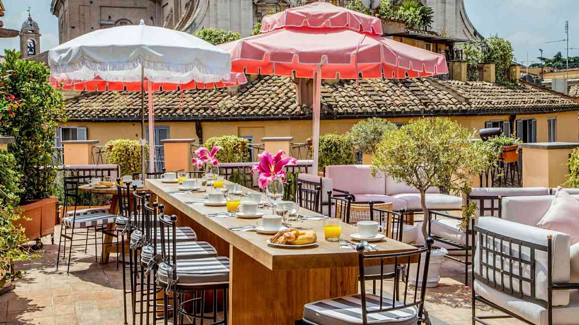 Terassi, jossa istuinryhmiä, aamiaistarjoilua ja aurinkovarjoja aurinkoisessa säässä. (Tekoälyn luoma teksti)