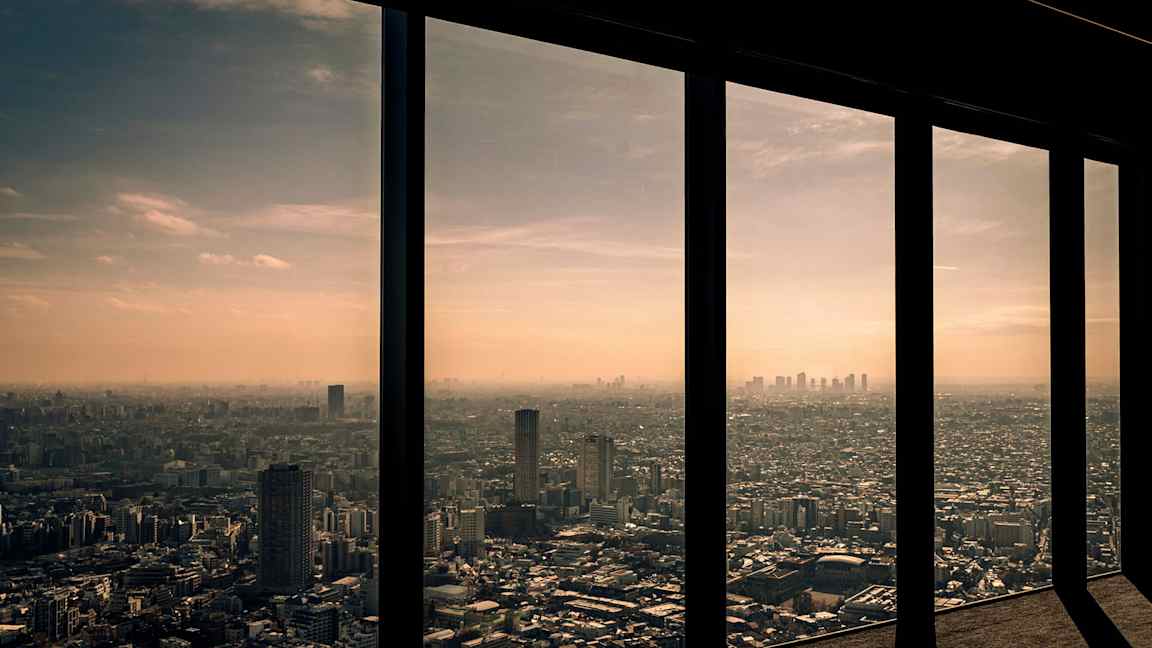 Näkymä kaupunkiin korkeiden ikkunoiden läpi auringonlaskun taustalla. (Tekoälyn luoma teksti)