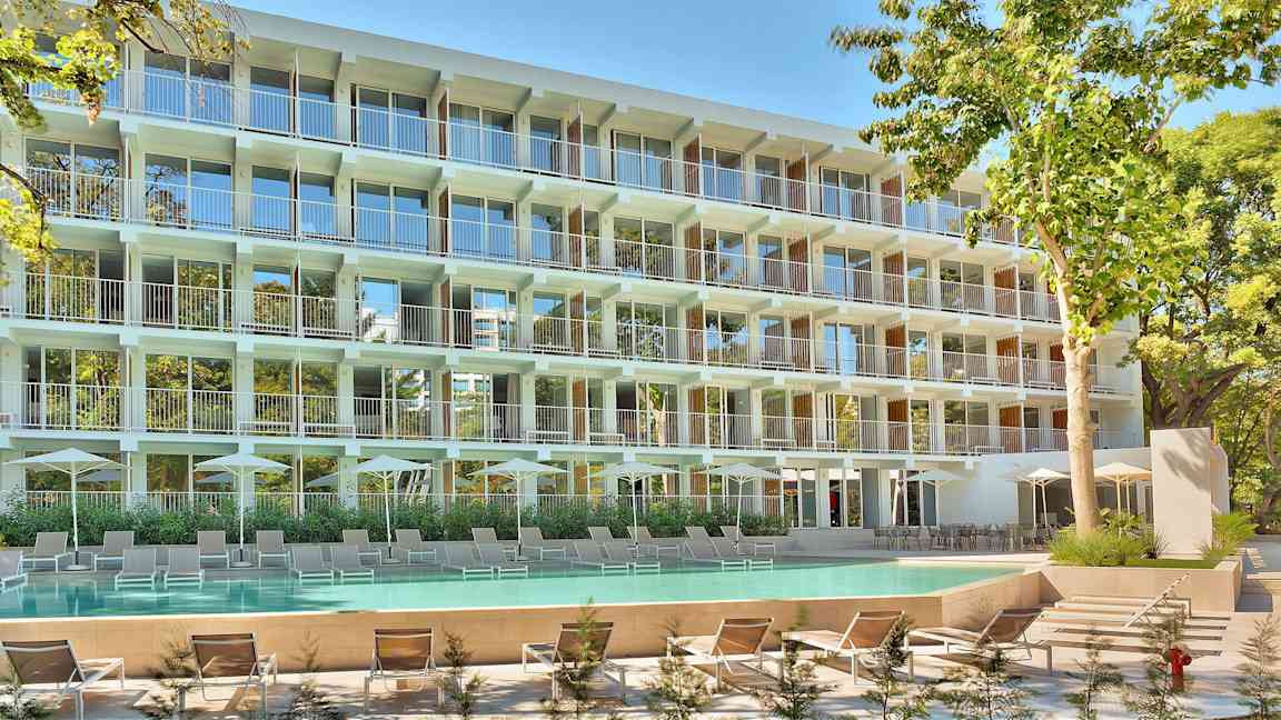 Monikerroksinen rakennus parvekkeilla, edessä pitkä allas ja aurinkotuoleja. (Tekoälyn luoma teksti)