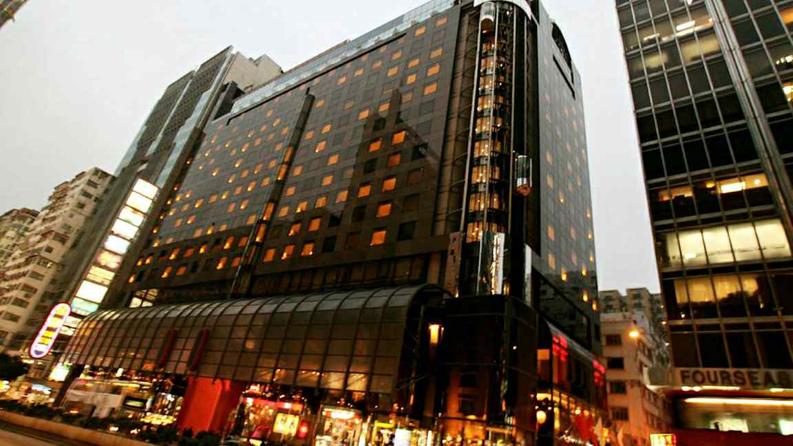 Valaistu monikerroksinen rakennus kaupunkimiljöössä, jossa on lasijulkisivu ja etualalla katuelämää. (Tekoälyn luoma teksti)