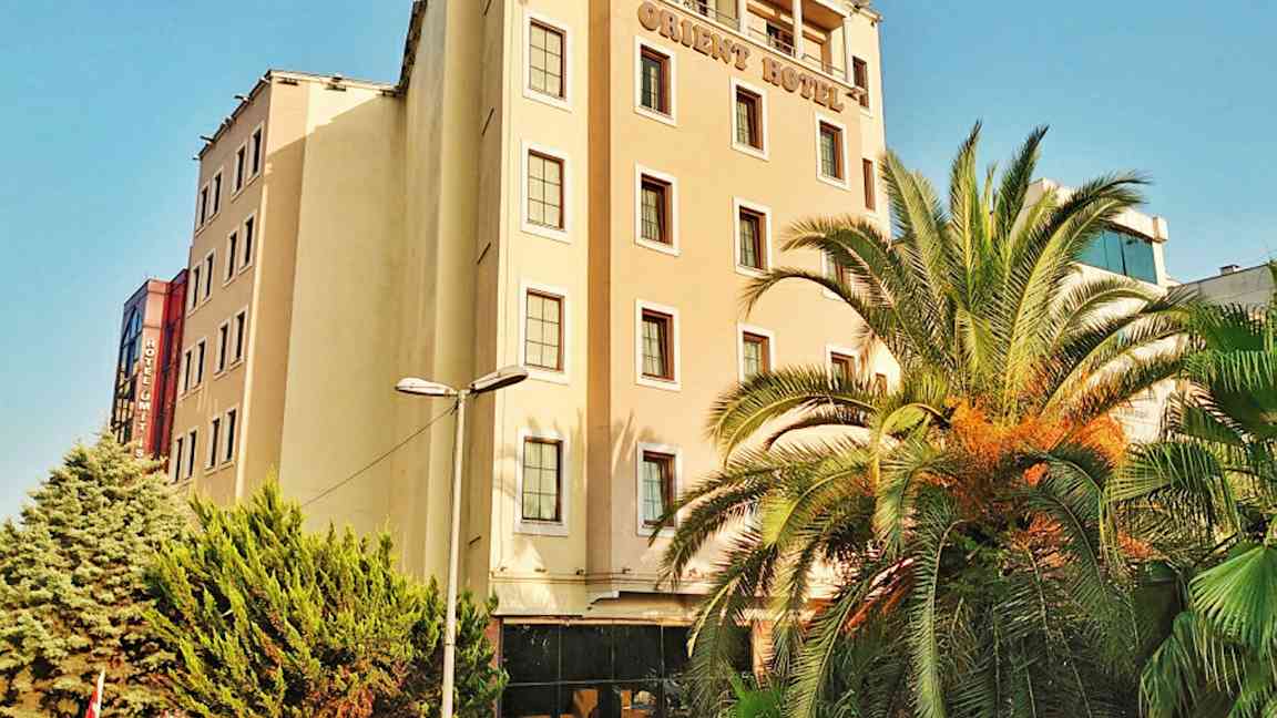 Monikerroksinen hotellirakennus. Rakennuksen edessä on palmuja ja vihreitä puita. (Tekoälyn luoma teksti)