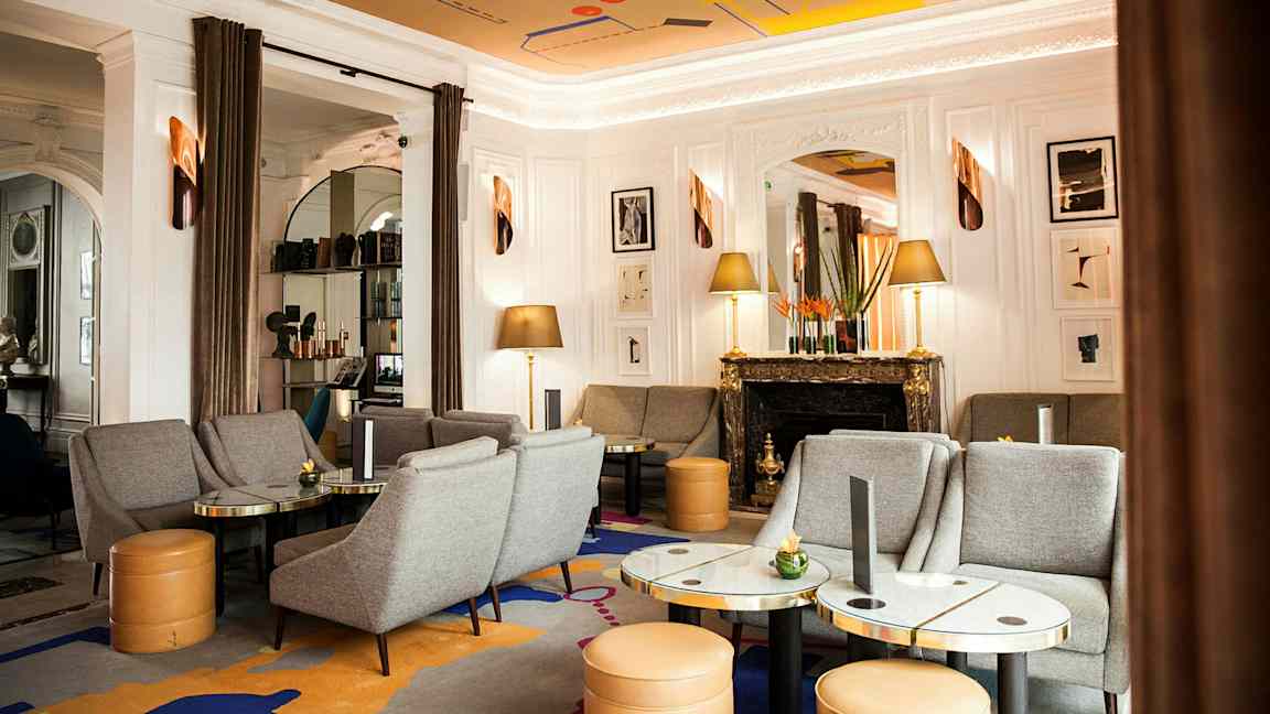 Tyylikäs olohuone, jossa harmaita sohvia ja nojatuoleja, marmorisia pöytiä, koristeellinen takka ja taideteoksia seinällä. (Tekoälyn luoma teksti)