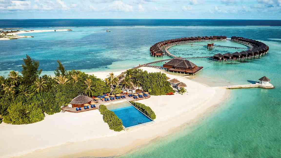 Ilmakuva trooppisesta rannikosta hiekkarannalla, merellä ja veden yläpuolisilla bungaloweilla. (Tekoälyn luoma teksti)