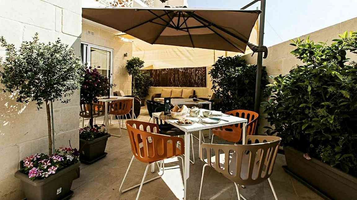 Terassi, jossa on ulkokalusteita, varjoja ja kasveja. (Tekoälyn luoma teksti)