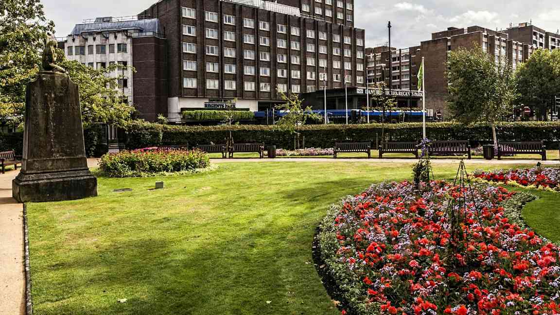 Puutarha, jossa kukkia ja nurmikko rakennuksen edessä. (Tekoälyn luoma teksti)