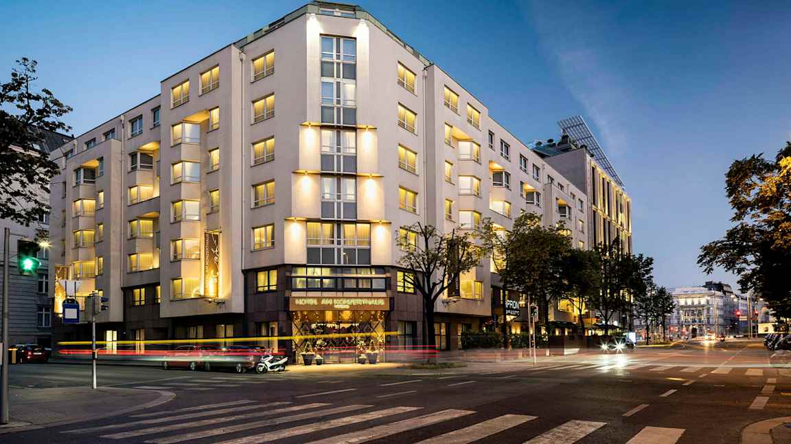 Rakennus valaistuna illalla, useita kerroksia ja ikkunoita, sijaitsee risteyksessä. (Tekoälyn luoma teksti)