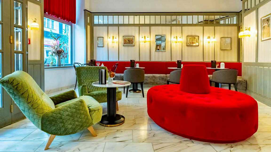 Hotelliaula, jossa istuinryhmä, mukaan lukien vihreät nojatuolit, punaiset ja harmaat istuinkalusteet sekä marmorilattia. (Tekoälyn luoma teksti)